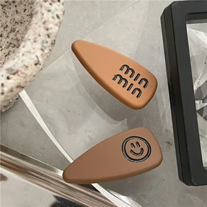 Macro shot of matte brown hair clips featuring 'min min' text and smiley face on stand