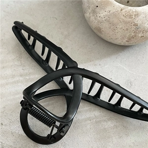 Detailed close-up of matte black hair claw clip with strong metal spring on stone texture