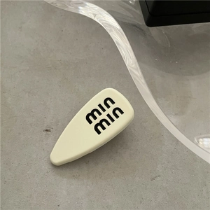 Macro shot of cream matte teardrop hair clip with min min letter print on stone surface