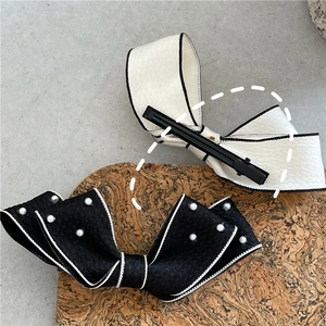 Detail of fabric bow hair clips with pearls and black duckbill clip on cork background