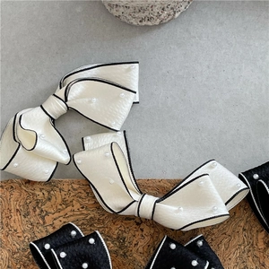 Detail of elegant satin bow hair clips with white pearls and chic black trim edges
