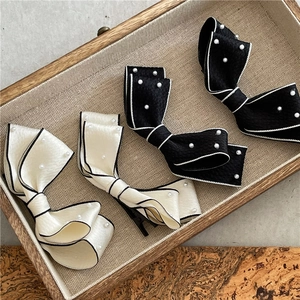Detailed view of pearl-embellished bow hair clips in elegant cream and black silk fabric