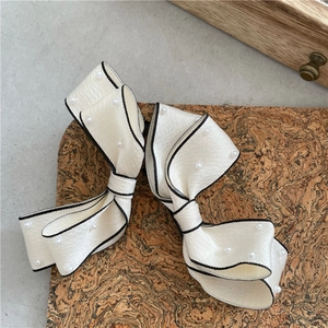 Detailed macro of cream satin bow hair clip with black edges and white pearl beads