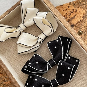 Detail of cream and black pearl bow hair clips with textured fabric and contrast piping