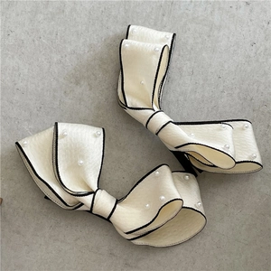 Detail of cream bow hair clips with faux pearls and black piping on elegant satin fabric