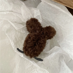 Detailed close-up of a brown fluffy teddy bear hair claw clip on white textured paper
