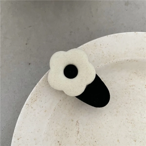 Close-up of a cute plush flower hair clip with cream petals and a black center dot