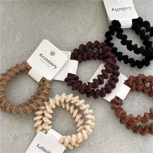 Dettaglio di cinque elastici per capelli a spirale in toni neutri su cartoncino