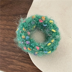 Close-up of green plush knit hair scrunchie with colorful spots on a rustic wooden desk