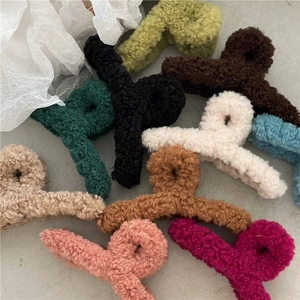Multiple colors of large fuzzy lamb wool hair claw clips set against a textured background