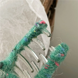 Détail de la pince à cheveux en laine tricotée verte avec des mouchetures colorées et dents