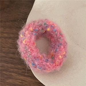 Detail of pink plush donut hair tie with colorful accents on a ceramic plate