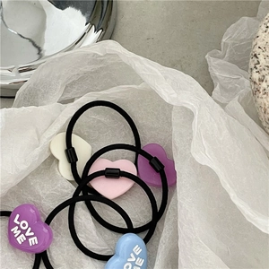 Detailed close-up of colorful heart hair ties with LOVE ME engraving on white paper