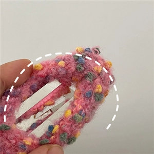 Close-up of pink knitted donut hair clip with colorful pompoms and metal BB clip