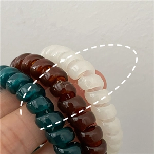 Close-up of spiral phone cord hair ties in teal, amber brown, and cream white colors