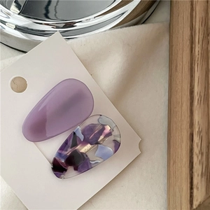 Close-up of acetic acid hair clips in solid purple and artistic marble texture on card