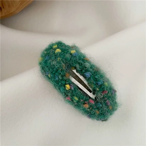 Close-up of green plush donut hair clip with colorful knitted spots and silver metal base