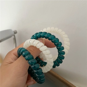Detail view of dark green and cream elastic telephone wire hair ties held by a person