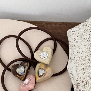 Detail view of four acetate heart hair ties with rhinestones on a ceramic tray