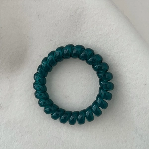 Close-up of a dark teal translucent spiral telephone cord hair tie on felt background