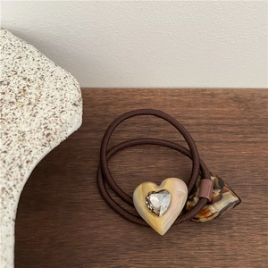 Macro view of brown elastic hair tie with cream acetate heart pendant and clear rhinestone