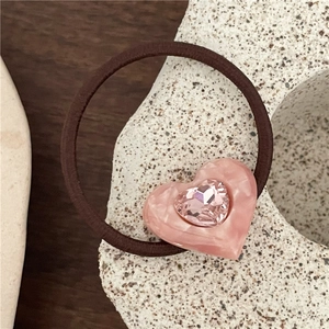 Detail shot of a pink acetate heart hair tie with a sparkling central crystal on a stone base