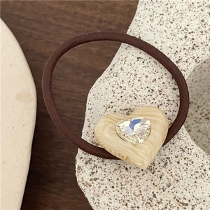Detail view of heart-shaped cream acetate hair tie with a sparkling central rhinestone