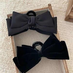 Detailed close-up of black velvet and satin bow hair clips in a wooden tray