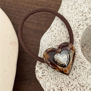 Macro shot of acetic acid heart hair tie with centered rhinestone on stone stand