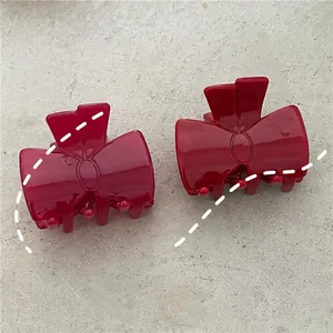 Close-up of two bright red acetic acid bow hair clips with glossy finish on stone surface
