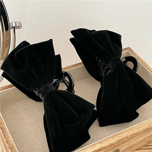 Close-up of elegant black velvet bow hair clips on a wooden tray for styling