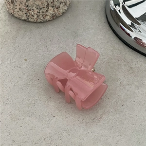 Detail of pink acetate bow hair clip with gold lettering on a grey textured surface