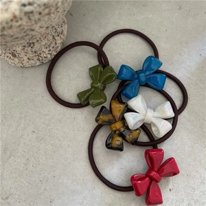 Detail view of five assorted acetate bow hair ties in green, blue, white, and red colors