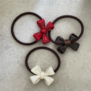 Three-piece acetate bow hair ties in red, brown, and pearl white on stone texture