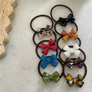 Set of ten colorful acetate bow hair ties in assorted patterns on a minimalist stone surface