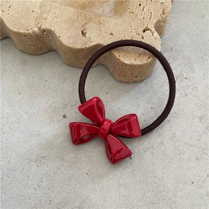 Close-up of a red acetate bow hair tie resting on a beige stone tray in soft lighting