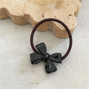 Detail of glossy black acetate bow hair tie on a decorative stone tray background