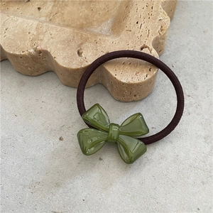 Close-up of elegant acetate bow hair tie in dark green on a textured tray
