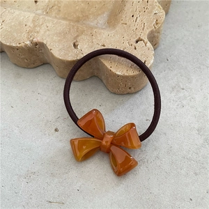 Detail of an amber acetate bow hair tie with a high-elastic brown rubber band on a stone surface