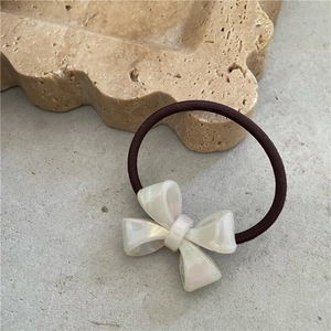 Close-up of cream acetate bow hair tie with pearl finish on a minimalist stone tray