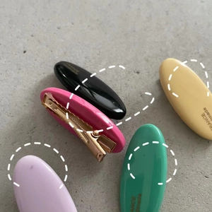 Detail showing five colorful resin oval hair clips with golden metal duckbill grips