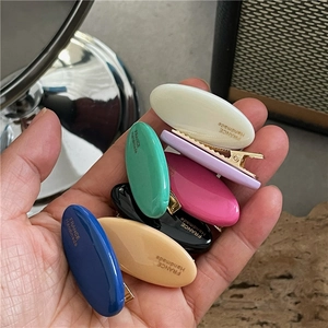 Detail of colorful oval hair clips with gold metal base and handmade text engraving