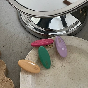 Colorful oval resin hair clips set with gold lettering in a white ceramic tray