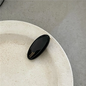 Detail of a handmade black oval hair clip with gold lettering on a ceramic plate