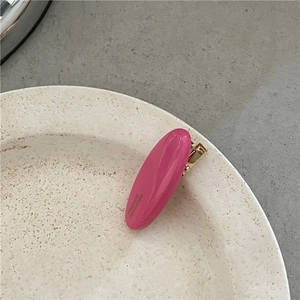 Detail view of a bright pink oval hair clip with gold metal base on a white ceramic plate