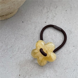Gros plan d'un charme fleur en résine jaune à texture d'encre sur un élastique à cheveux