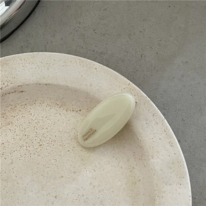Close-up of handmade cream oval acetate hair clip with gold France lettering on ceramic dish