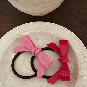 Détail d'élastiques à cheveux nœud en acétate rose et fuchsia avec texte doré sur un plateau