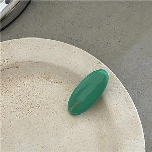 Macro shot of a minimalist bright green oval hair clip on a textured ceramic plate