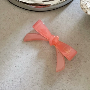Détail de la pince à cheveux nœud en acétate rose avec lettrage doré sur fond de pierre